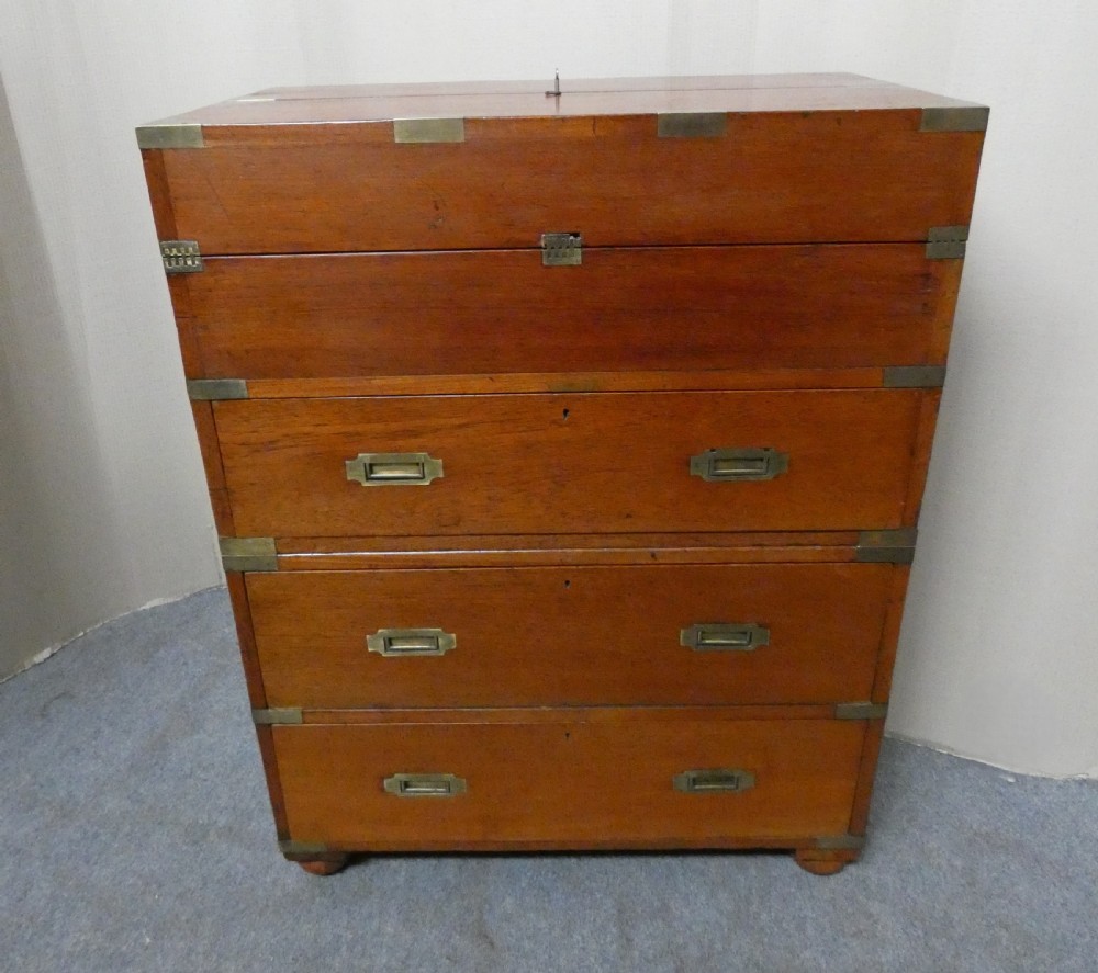 An antique teak campaign secretaire chest featuring brass corner mounts, flush drawer handles, carrying handles, and a drop-front slanted leather writing desk. View X
