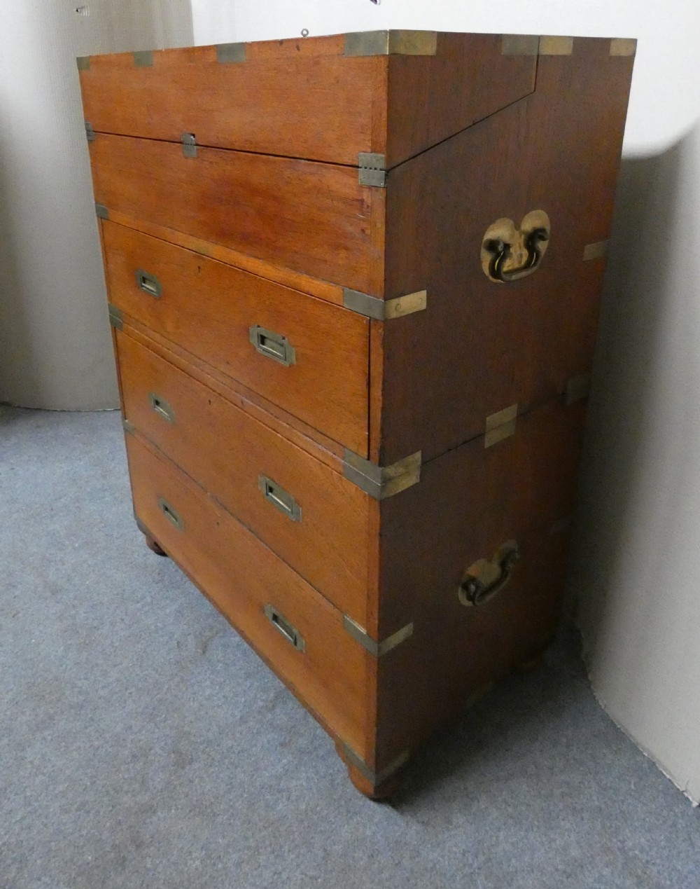 An antique teak campaign secretaire chest featuring brass corner mounts, flush drawer handles, carrying handles, and a drop-front slanted leather writing desk. View XI