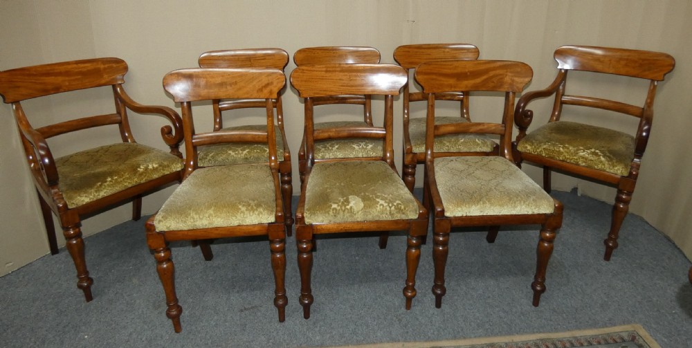 A set of eight antique mahogany dining chairs featuring curved bar backs, turned front legs, and mustard patterned fabric seats.