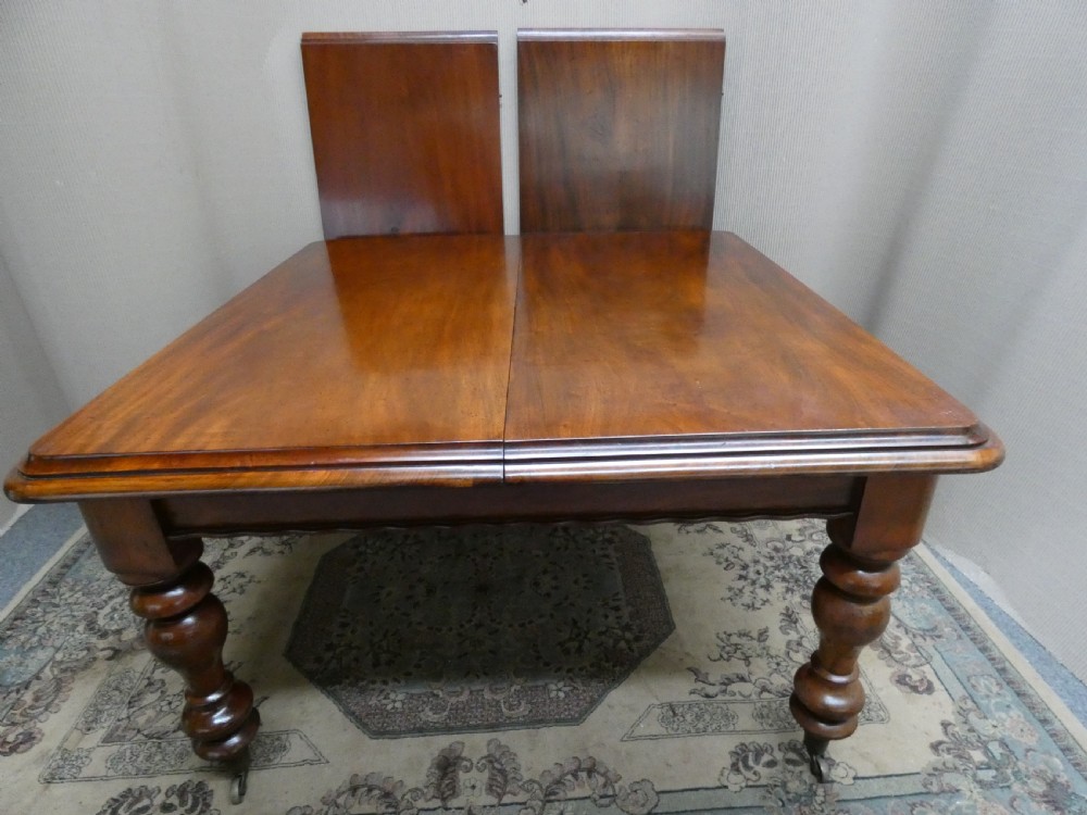 A rectangular mahogany extending dining table with two removable leaves displayed upright, resting on heavy turned legs with brass castors.