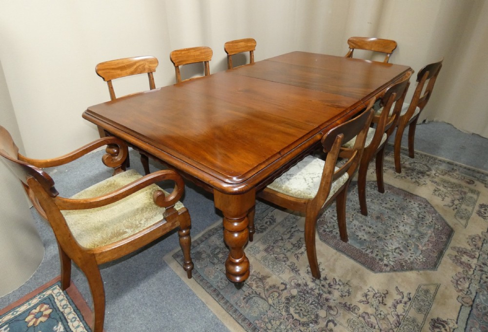 A rectangular mahogany extending dining table with two removable leaves displayed upright, resting on heavy turned legs with brass castors. View II