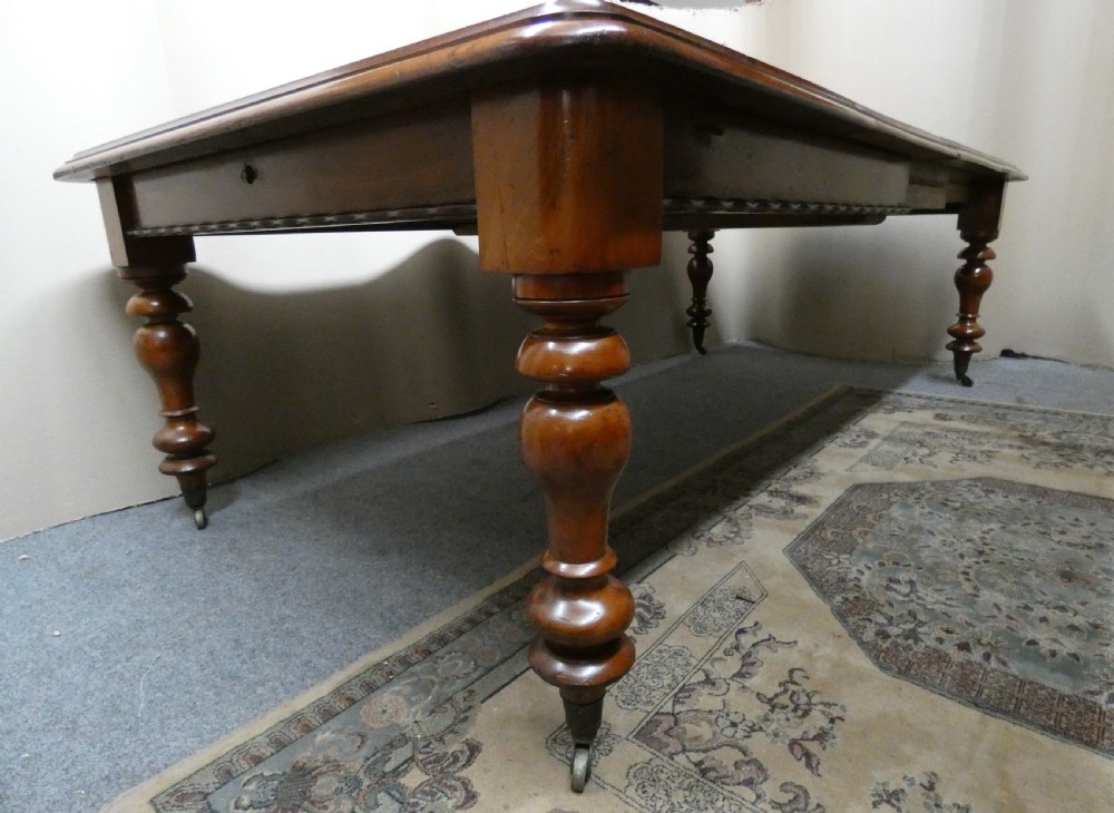 A rectangular mahogany extending dining table with two removable leaves displayed upright, resting on heavy turned legs with brass castors. View VI