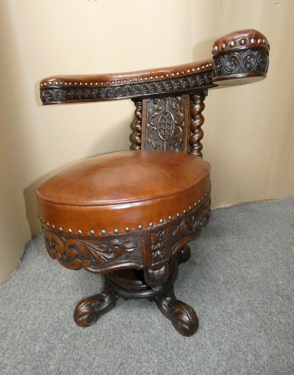 A carved dark oak cockfighting chair featuring tan leather upholstery with brass stud trimmings, a wide padded armrest, and barley twist support posts. View III
