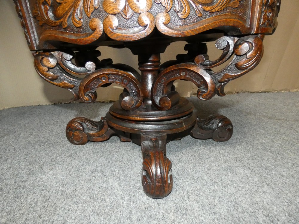 A carved dark oak cockfighting chair featuring tan leather upholstery with brass stud trimmings, a wide padded armrest, and barley twist support posts. View VI