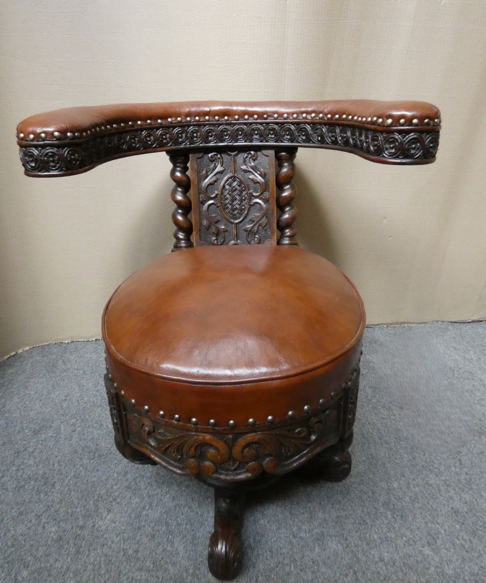 A carved dark oak cockfighting chair featuring tan leather upholstery with brass stud trimmings, a wide padded armrest, and barley twist support posts. View VII