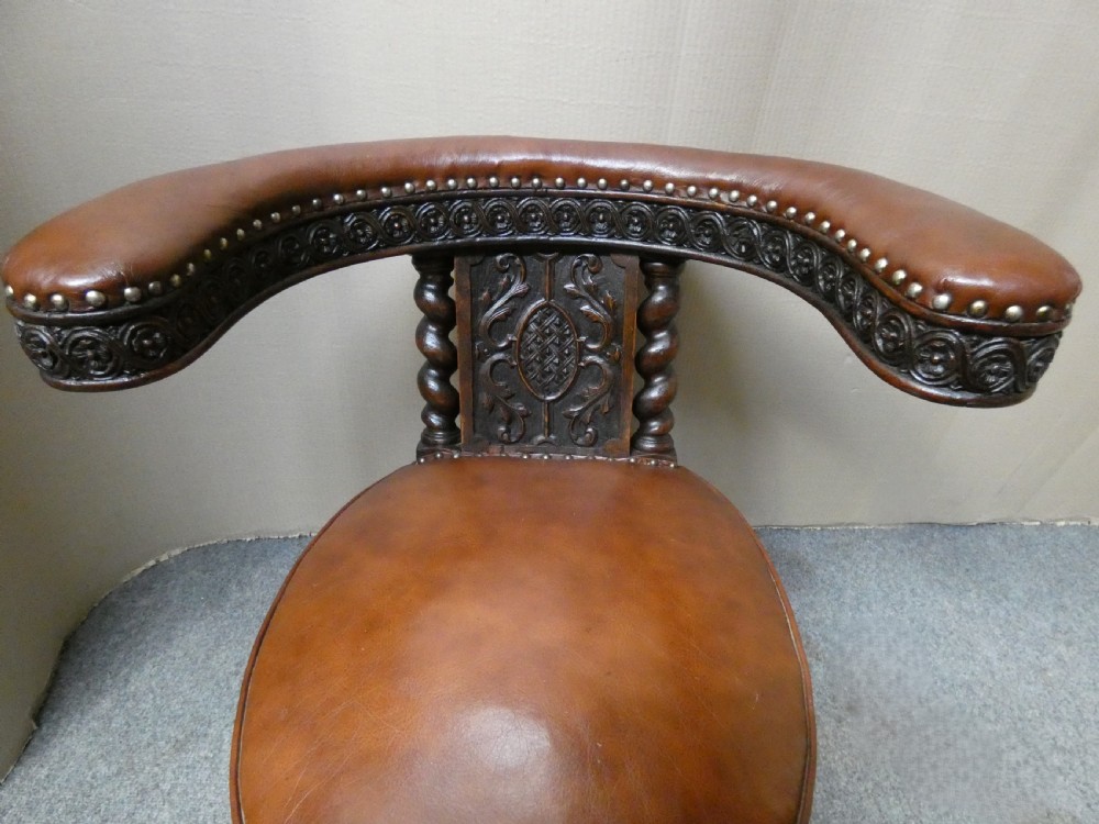 A carved dark oak cockfighting chair featuring tan leather upholstery with brass stud trimmings, a wide padded armrest, and barley twist support posts. View VIII