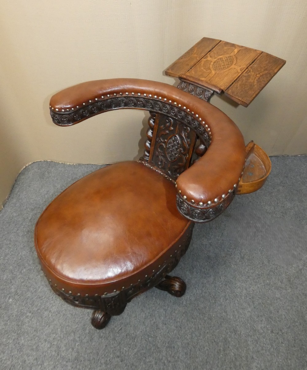 A carved dark oak cockfighting chair featuring tan leather upholstery with brass stud trimmings, a wide padded armrest, and barley twist support posts. View XI