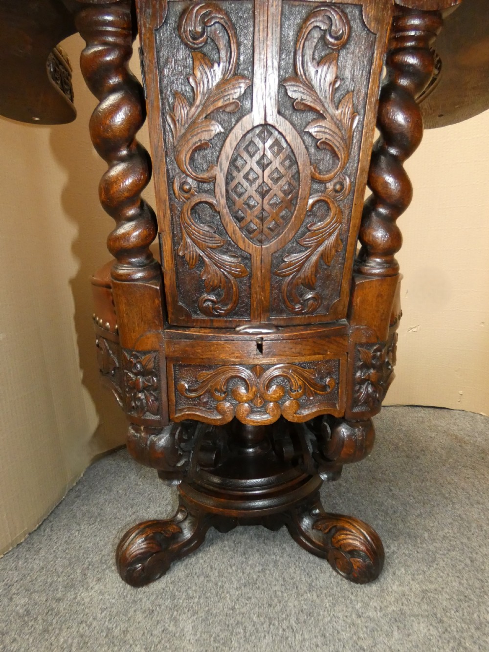 A carved dark oak cockfighting chair featuring tan leather upholstery with brass stud trimmings, a wide padded armrest, and barley twist support posts. View XII