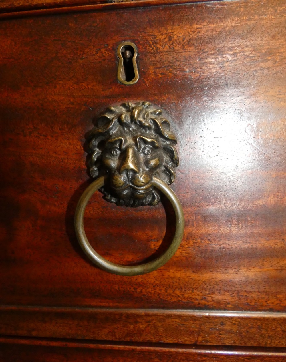 A Regency mahogany linen press featuring an arched pediment, twin panelled doors with geometric stringing, and a lower section with four drawers fitted with brass lion mask ring handles. View VI