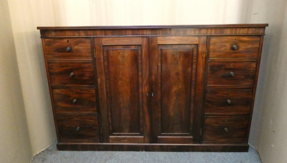 A Georgian mahogany low linen press featuring two central panelled doors flanked by eight side drawers with turned wooden knobs.