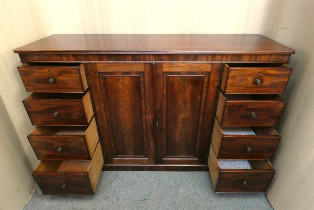A Georgian mahogany low linen press featuring two central panelled doors flanked by eight side drawers with turned wooden knobs. View V