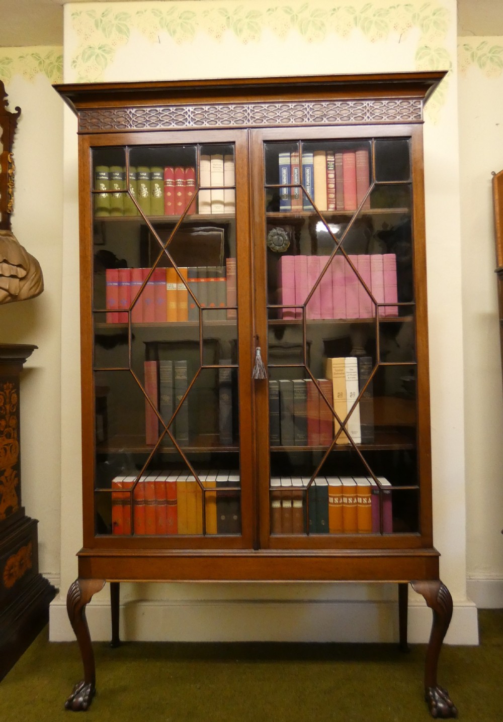 An antique mahogany bookcase featuring two astragal glazed doors, a carved fretwork frieze, and cabriole legs with claw and ball feet.