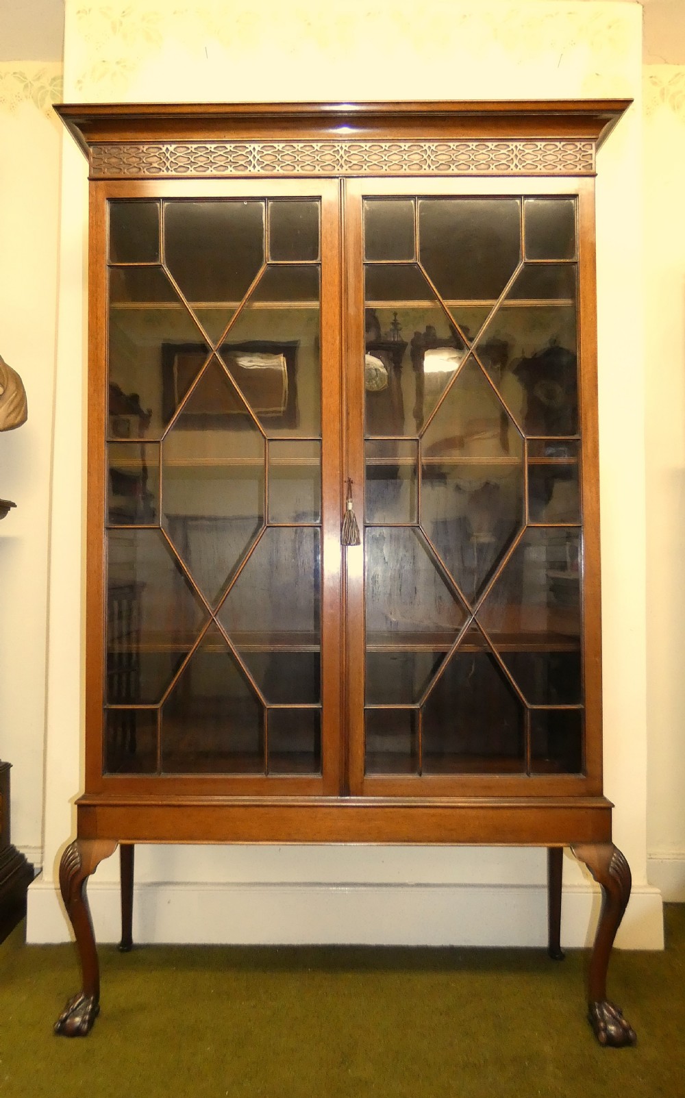 An antique mahogany bookcase featuring two astragal glazed doors, a carved fretwork frieze, and cabriole legs with claw and ball feet. View II