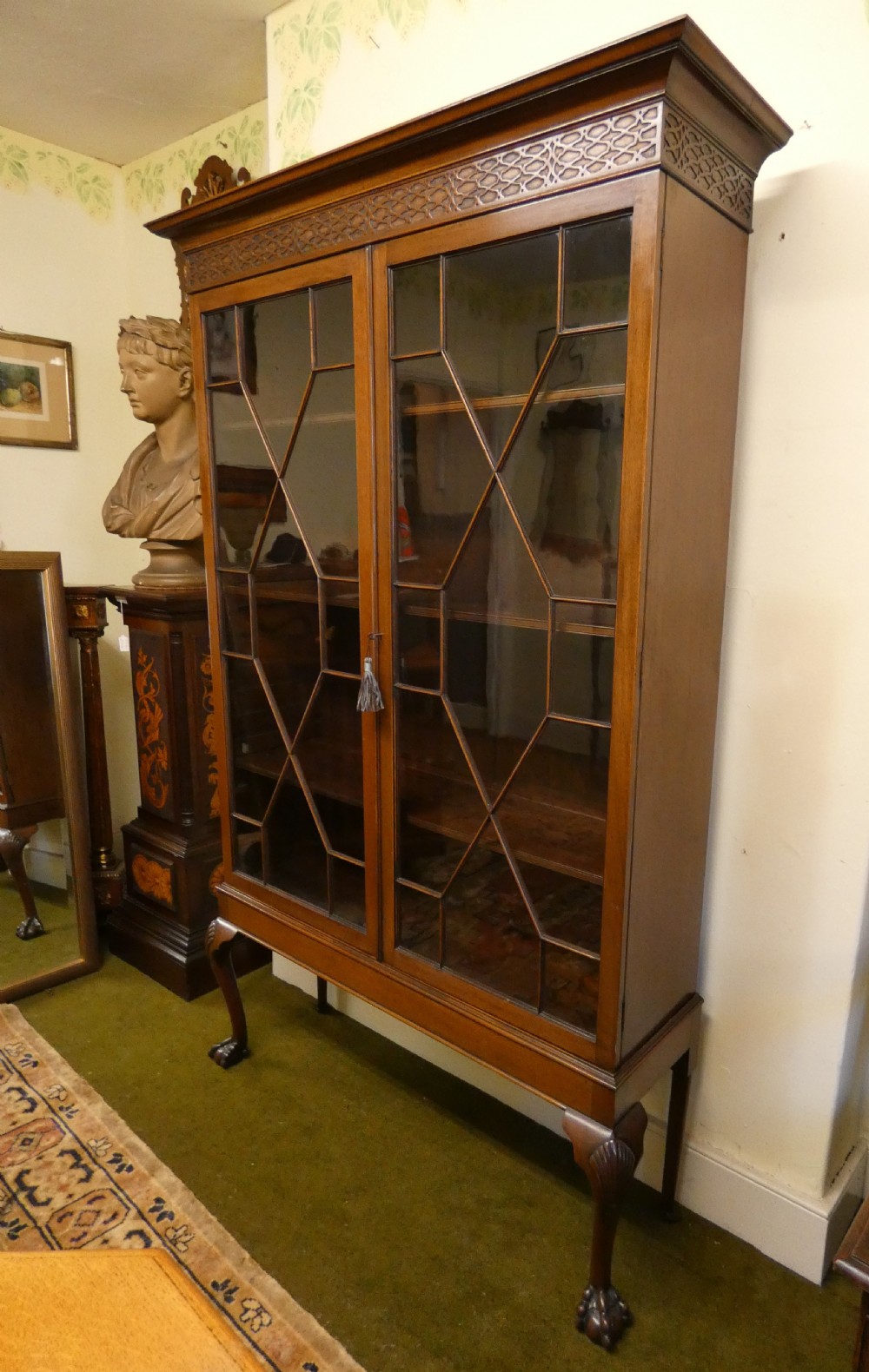 An antique mahogany bookcase featuring two astragal glazed doors, a carved fretwork frieze, and cabriole legs with claw and ball feet. View III