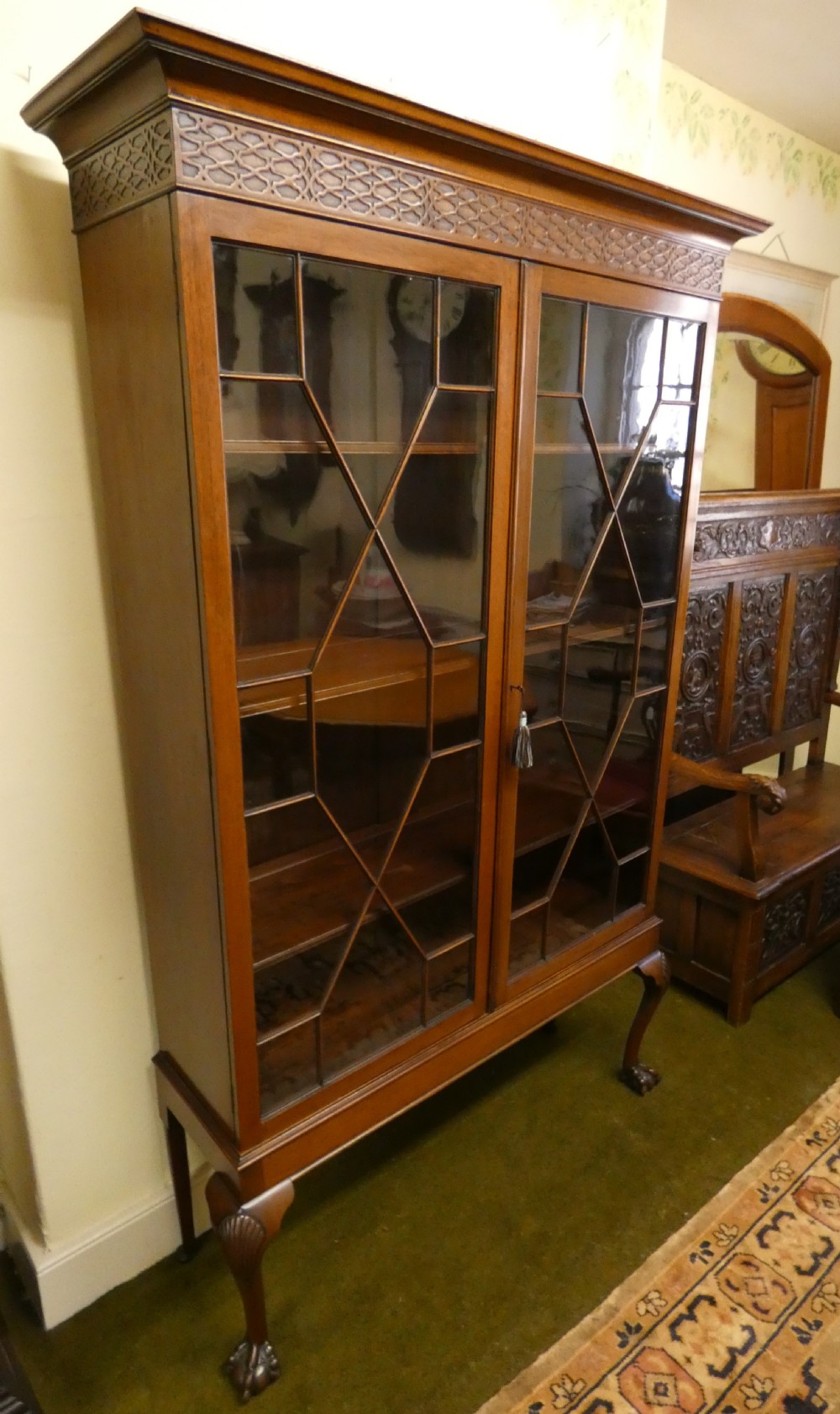 An antique mahogany bookcase featuring two astragal glazed doors, a carved fretwork frieze, and cabriole legs with claw and ball feet. View V