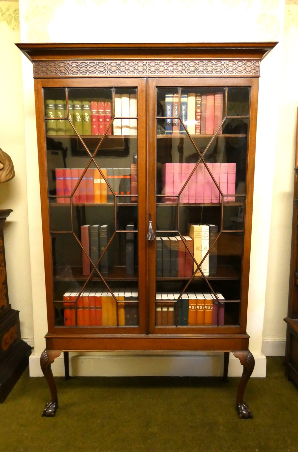 An antique mahogany bookcase featuring two astragal glazed doors, a carved fretwork frieze, and cabriole legs with claw and ball feet. View IX