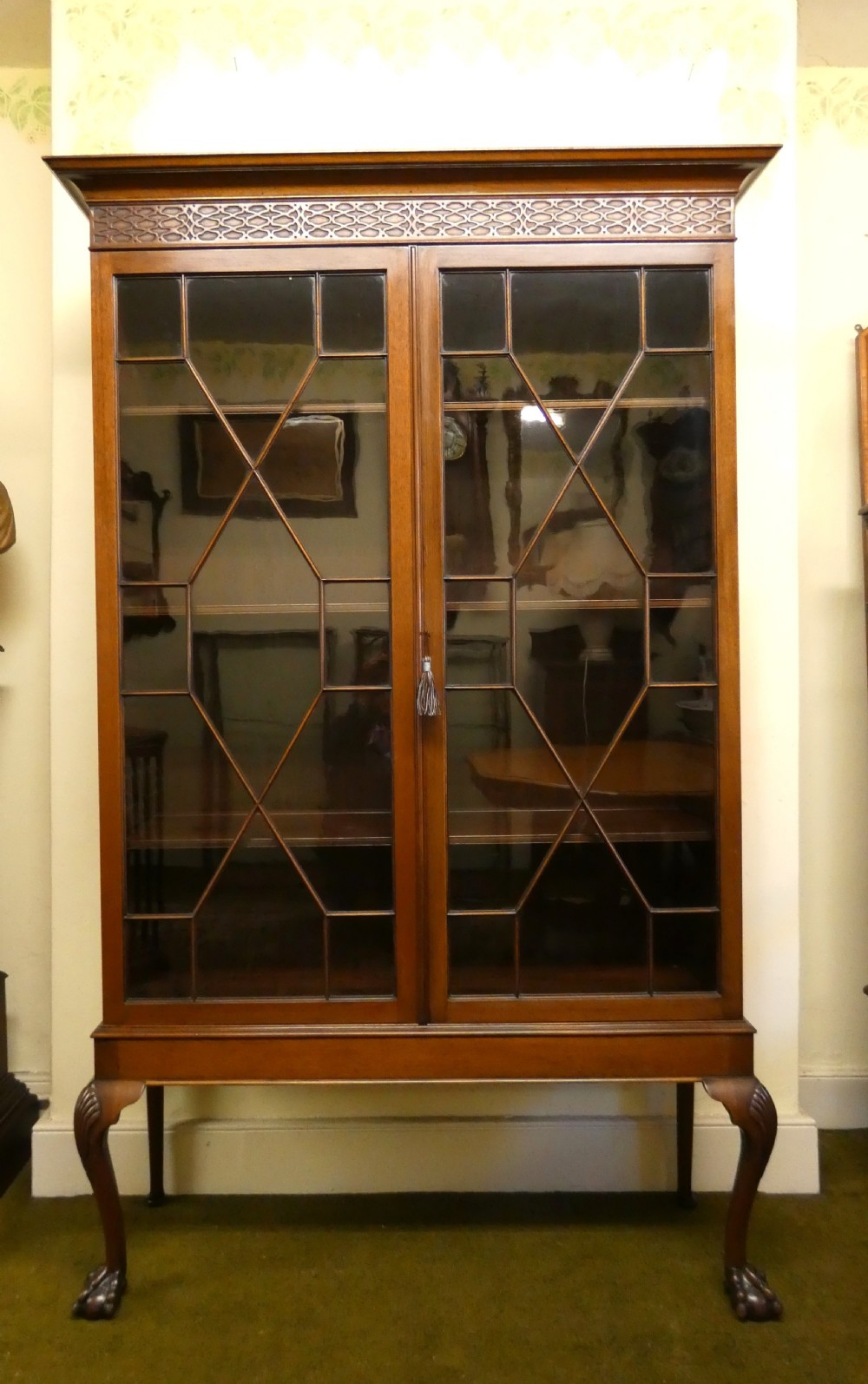 An antique mahogany bookcase featuring two astragal glazed doors, a carved fretwork frieze, and cabriole legs with claw and ball feet. View X