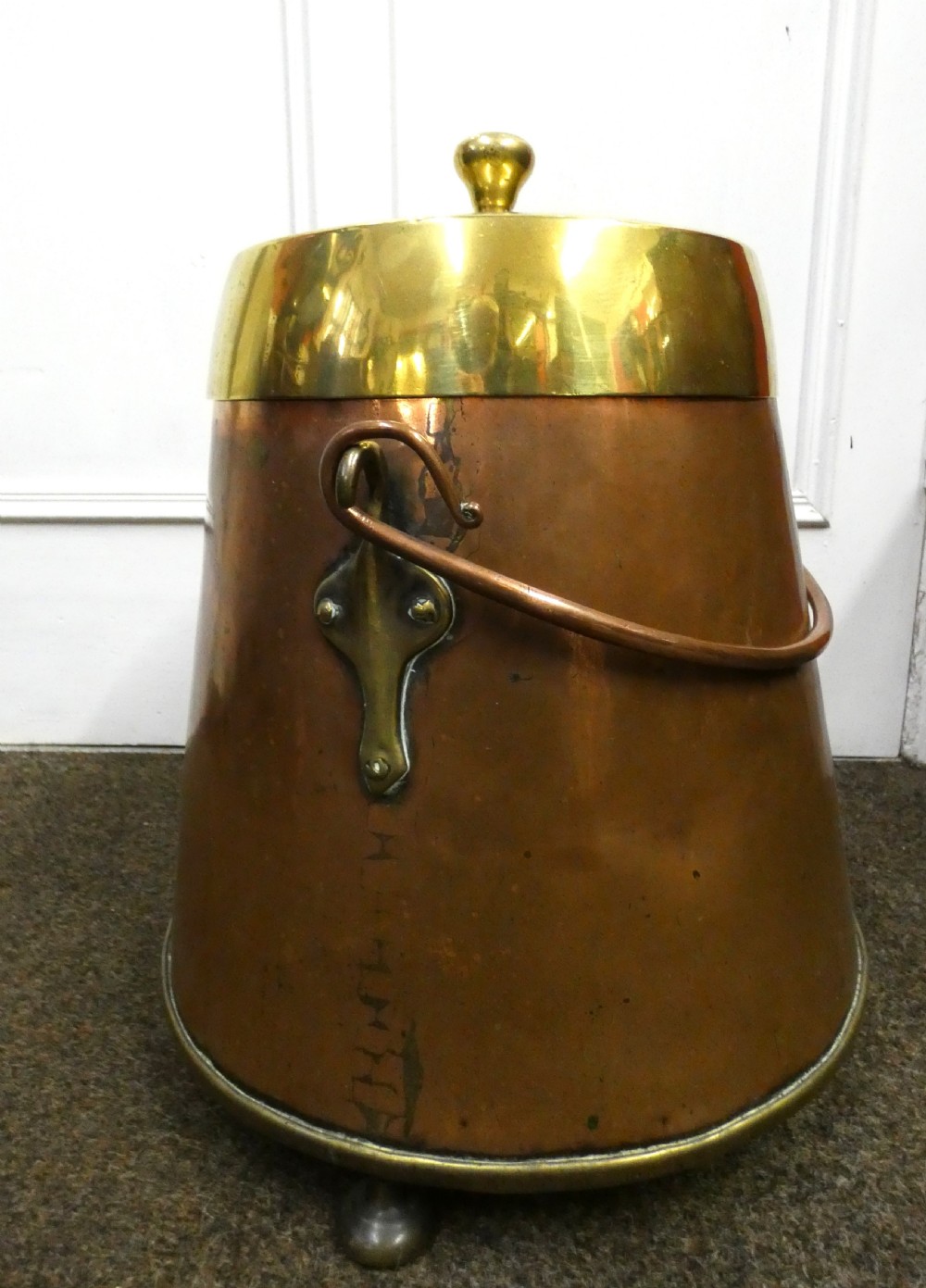 A tapered cylindrical copper coal bin featuring a polished brass collar and top finial, a copper swing handle, and decorative brass mounts. View II