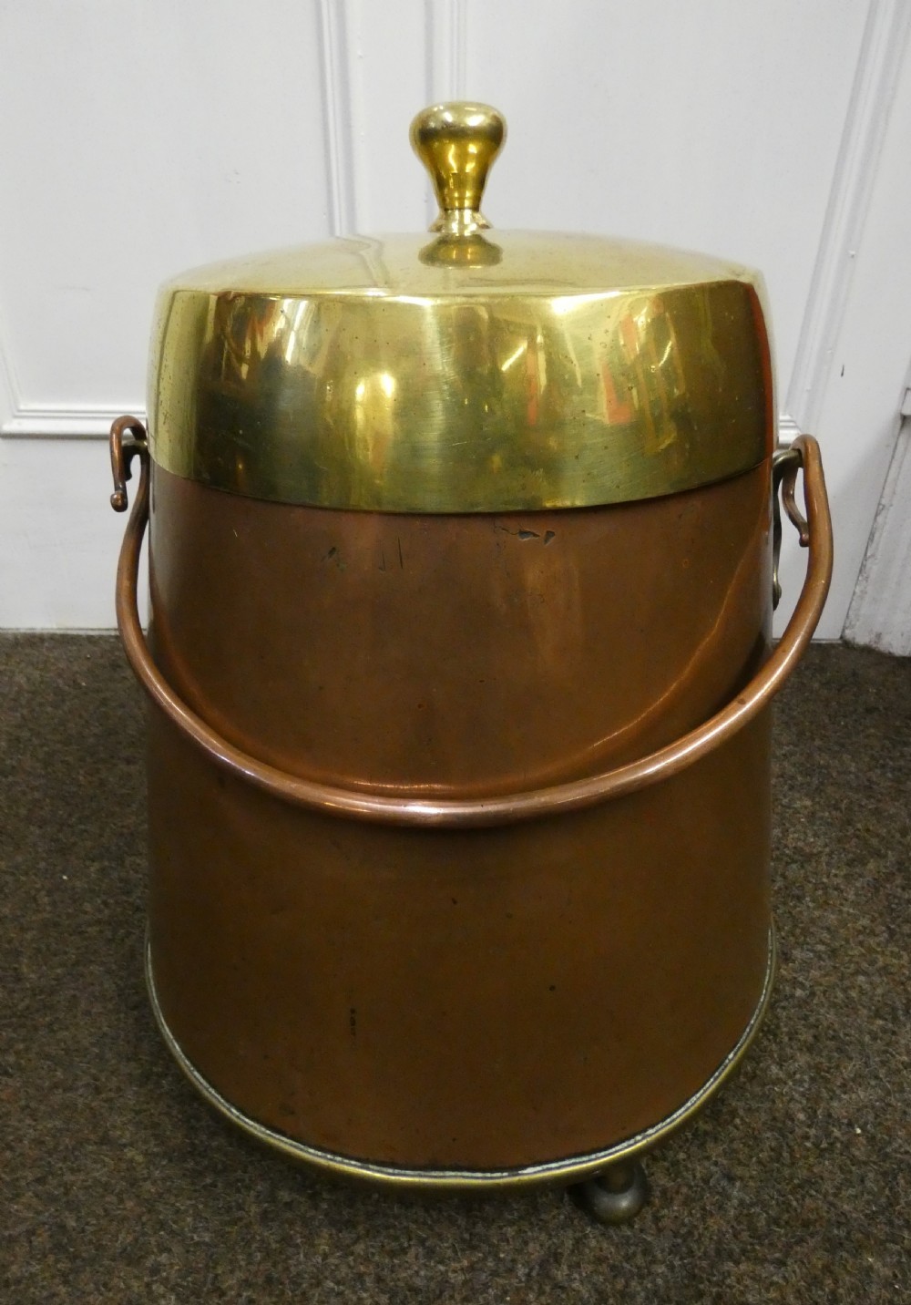 A tapered cylindrical copper coal bin featuring a polished brass collar and top finial, a copper swing handle, and decorative brass mounts. View V