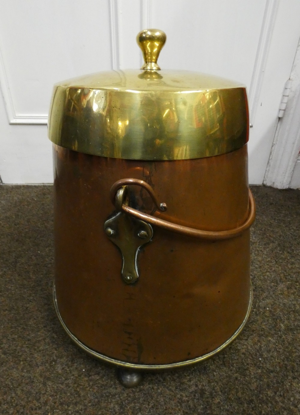 A tapered cylindrical copper coal bin featuring a polished brass collar and top finial, a copper swing handle, and decorative brass mounts. View VI