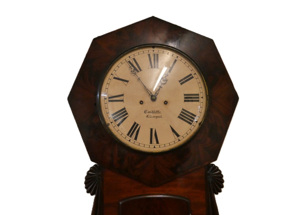 An antique mahogany tavern wall clock featuring an octagonal dial surround, carved side ears, and a long rectangular trunk with a flame mahogany door. View II