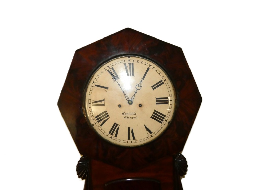 An antique mahogany tavern wall clock featuring an octagonal dial surround, carved side ears, and a long rectangular trunk with a flame mahogany door. View VI