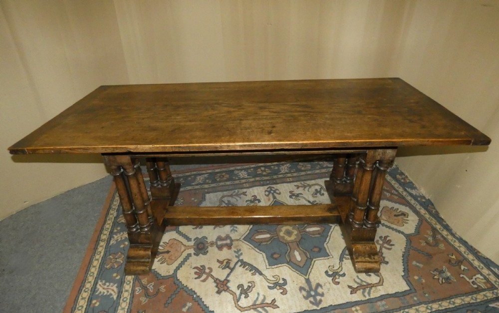 An antique oak refectory table featuring a rectangular top resting on clustered turned column trestle supports joined by a central floor stretcher.