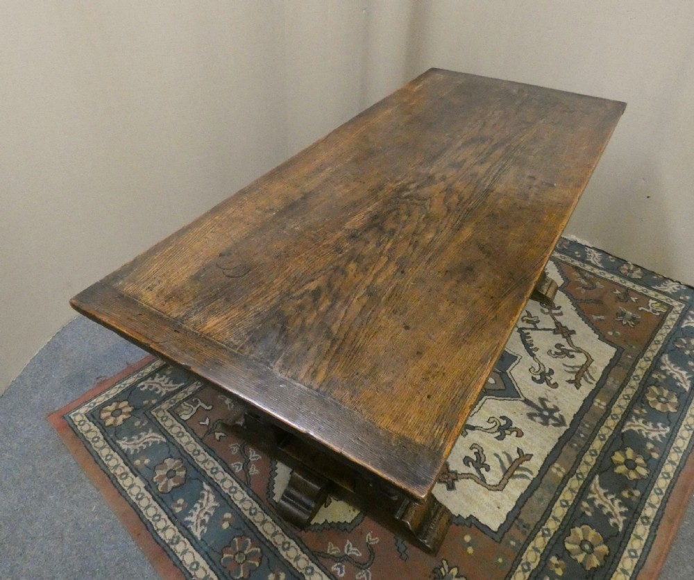 An antique oak refectory table featuring a rectangular top resting on clustered turned column trestle supports joined by a central floor stretcher. View III