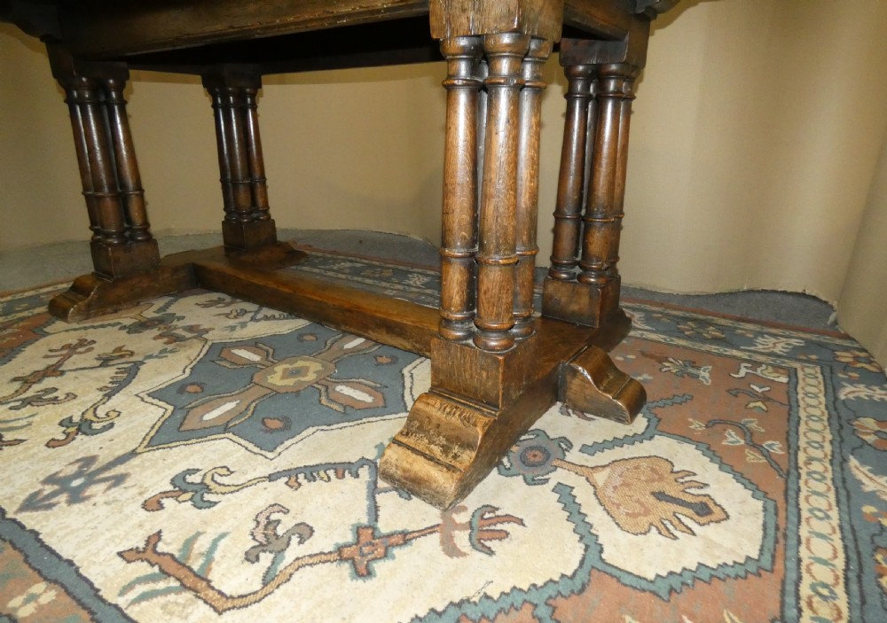 An antique oak refectory table featuring a rectangular top resting on clustered turned column trestle supports joined by a central floor stretcher. View V