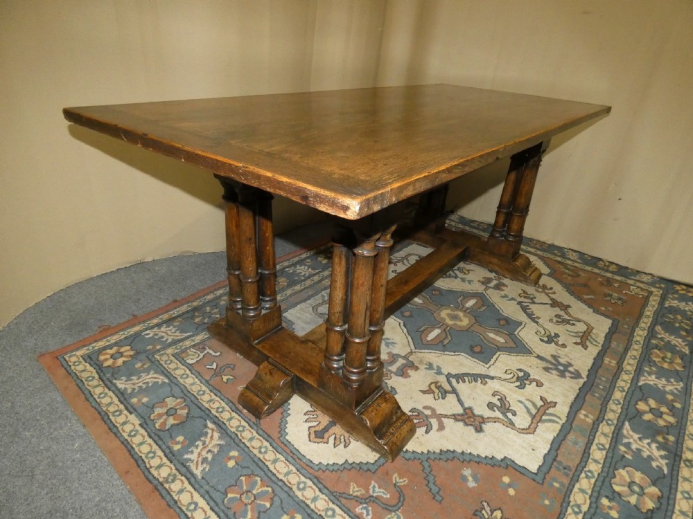 An antique oak refectory table featuring a rectangular top resting on clustered turned column trestle supports joined by a central floor stretcher. View VII