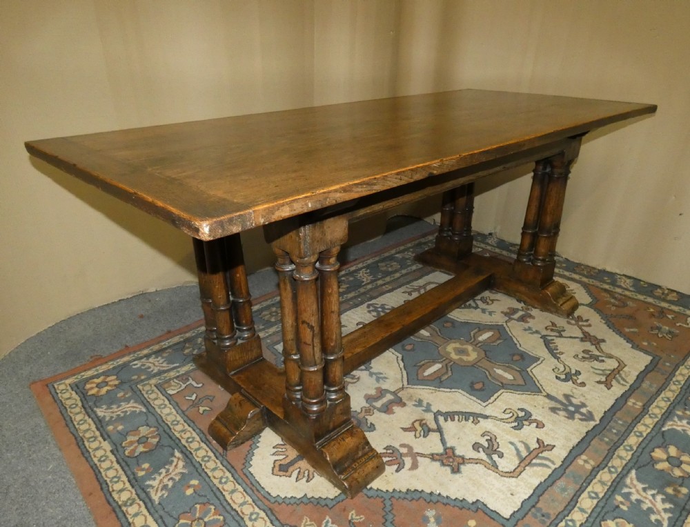 An antique oak refectory table featuring a rectangular top resting on clustered turned column trestle supports joined by a central floor stretcher. View VIII