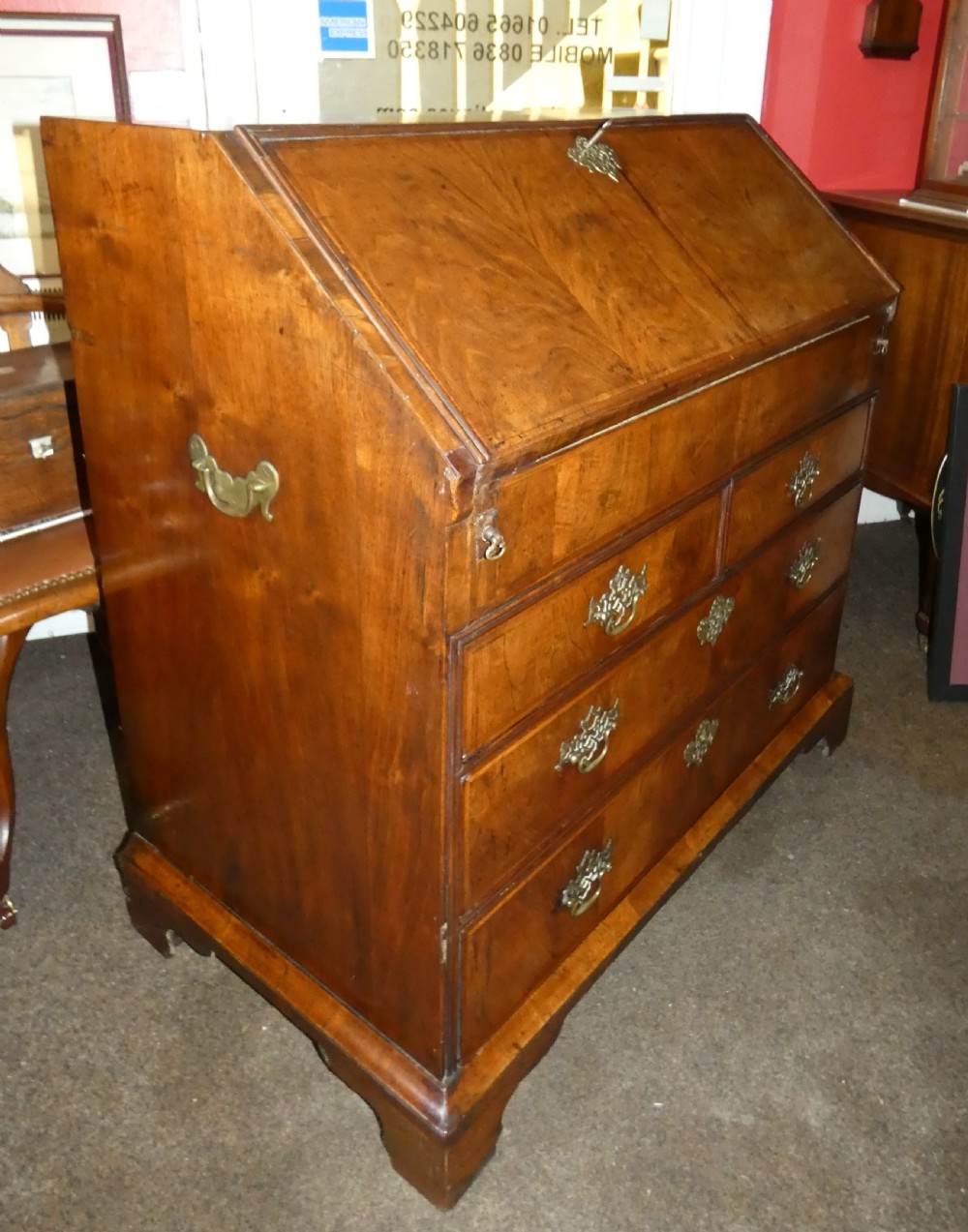 A George II period walnut slant-front bureau featuring figured veneers, brass drop handles, keyhole escutcheons, and graduating drawers on bracket feet. View II