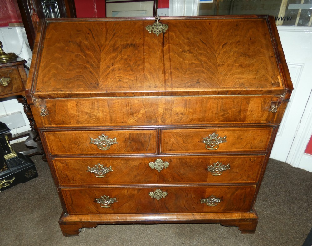A George II period walnut slant-front bureau featuring figured veneers, brass drop handles, keyhole escutcheons, and graduating drawers on bracket feet. View III