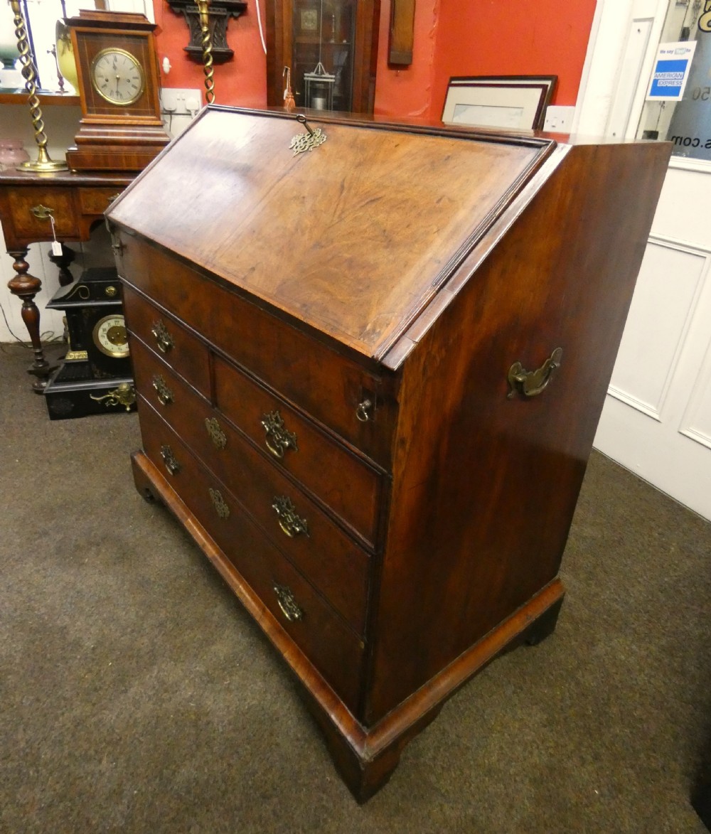 A George II period walnut slant-front bureau featuring figured veneers, brass drop handles, keyhole escutcheons, and graduating drawers on bracket feet. View IV