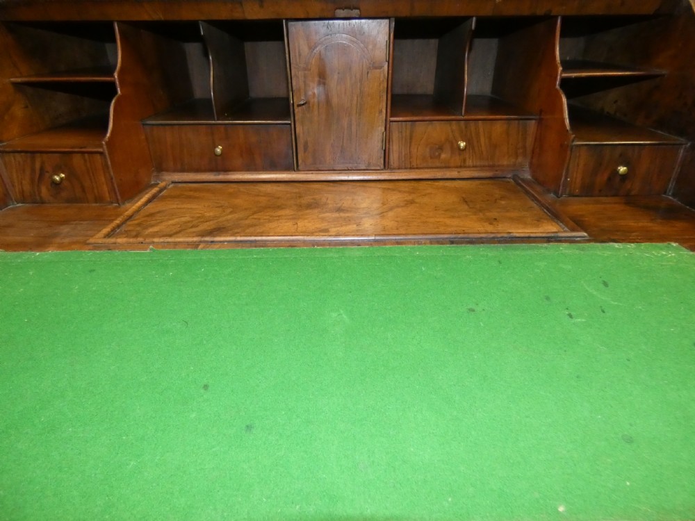 A George II period walnut slant-front bureau featuring figured veneers, brass drop handles, keyhole escutcheons, and graduating drawers on bracket feet. View V