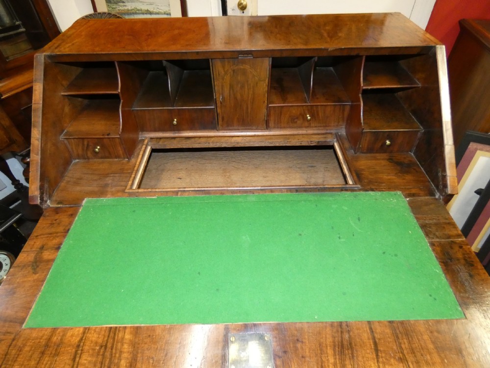 A George II period walnut slant-front bureau featuring figured veneers, brass drop handles, keyhole escutcheons, and graduating drawers on bracket feet. View VI
