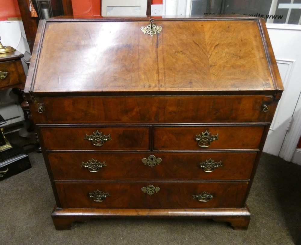 A George II period walnut slant-front bureau featuring figured veneers, brass drop handles, keyhole escutcheons, and graduating drawers on bracket feet. View VII