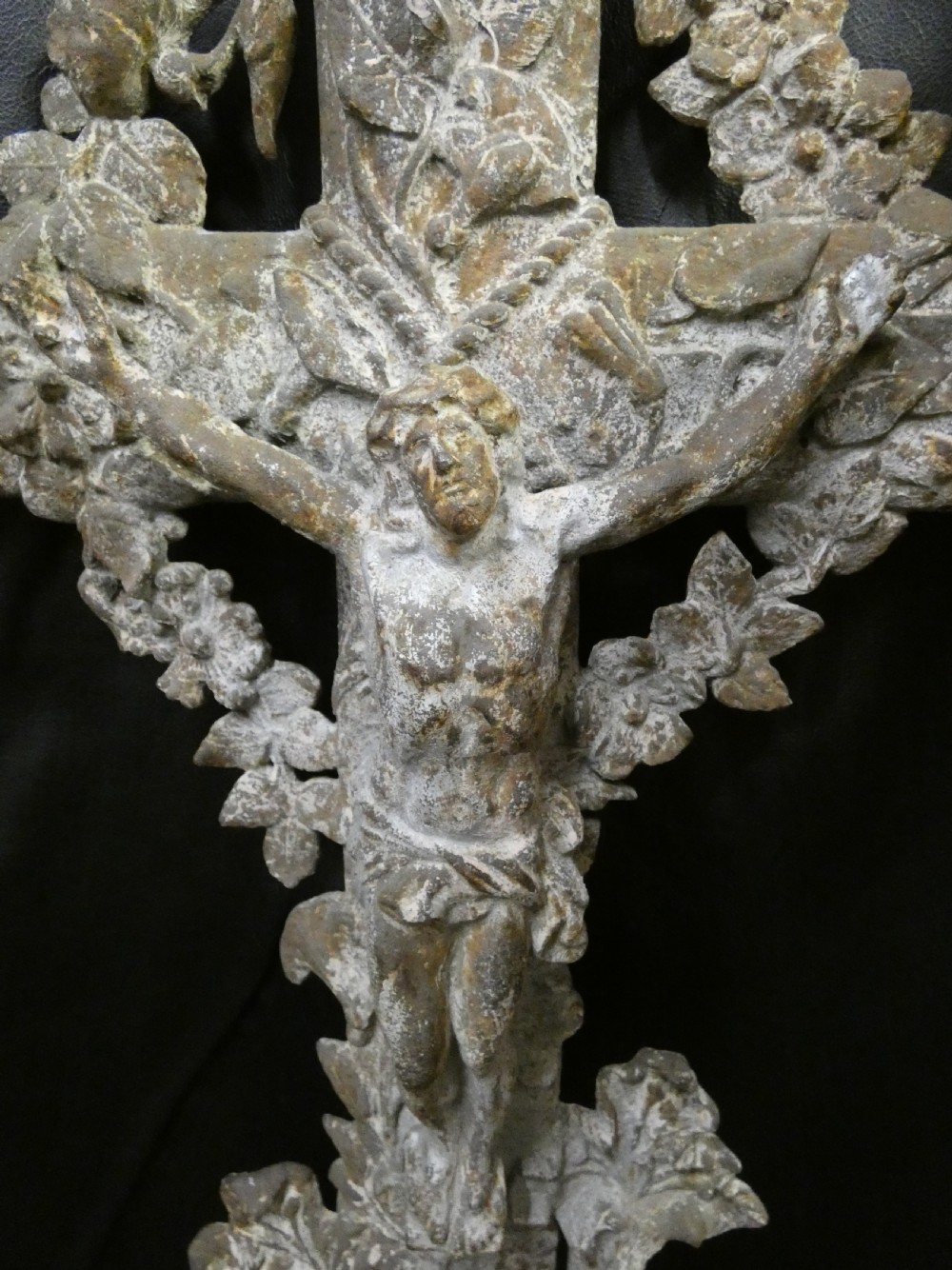 A weathered cast iron grave crucifix featuring detailed foliate work along the vertical beam and the figure of Christ in relief against a distressed grey finish. View III