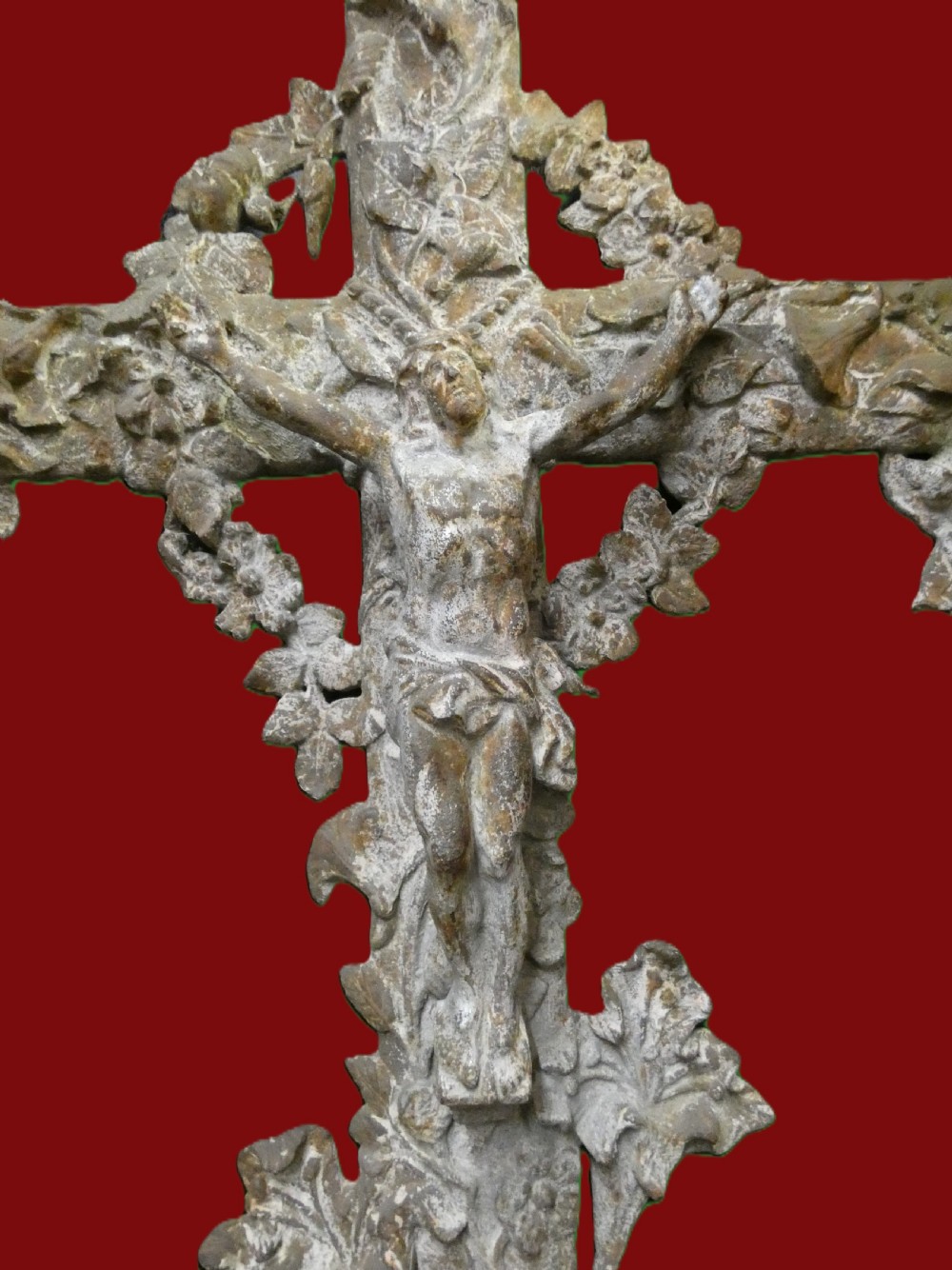 A weathered cast iron grave crucifix featuring detailed foliate work along the vertical beam and the figure of Christ in relief against a distressed grey finish. View IV