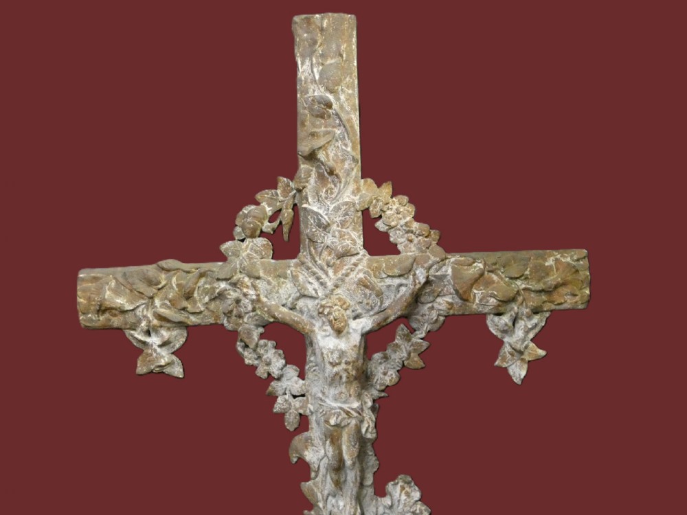 A weathered cast iron grave crucifix featuring detailed foliate work along the vertical beam and the figure of Christ in relief against a distressed grey finish. View V