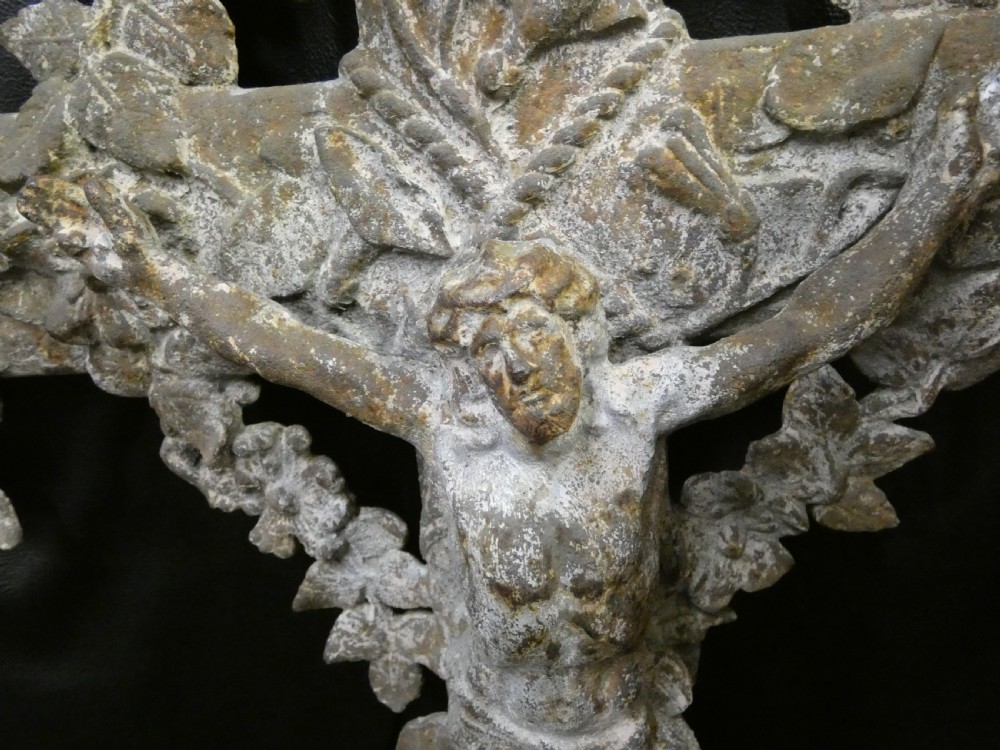 A weathered cast iron grave crucifix featuring detailed foliate work along the vertical beam and the figure of Christ in relief against a distressed grey finish. View VIII