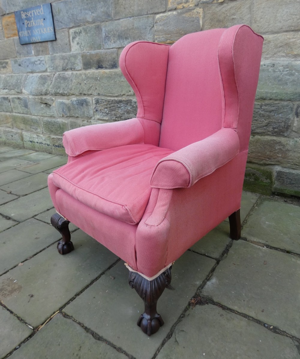 A 19th-century wingback armchair upholstered in rose pink fabric with carved mahogany cabriole front legs resting on ball-and-claw feet.