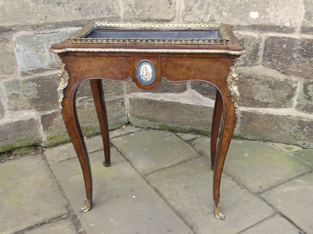 A French Louis XV style burr walnut jardiniere table with cabriole legs, ormolu mounts, a central porcelain plaque, and a brass gallery rim.