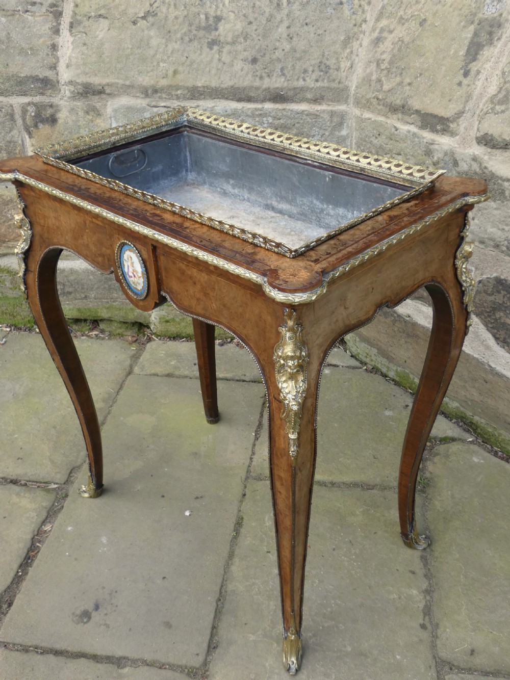 A French Louis XV style burr walnut jardiniere table with cabriole legs, ormolu mounts, a central porcelain plaque, and a brass gallery rim. View V