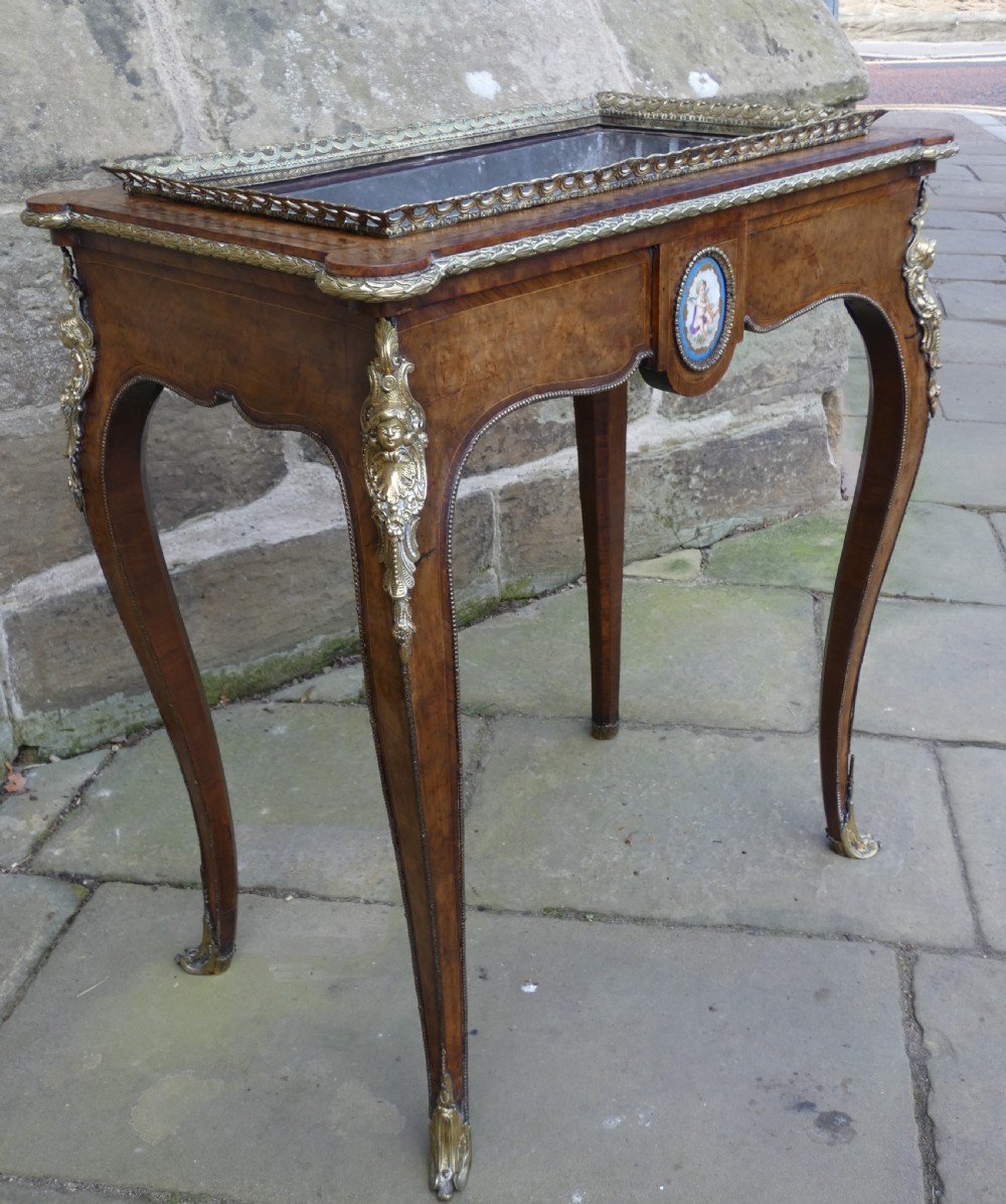 A French Louis XV style burr walnut jardiniere table with cabriole legs, ormolu mounts, a central porcelain plaque, and a brass gallery rim. View VI
