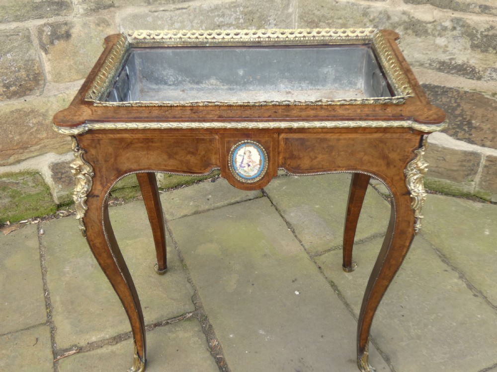 A French Louis XV style burr walnut jardiniere table with cabriole legs, ormolu mounts, a central porcelain plaque, and a brass gallery rim. View X