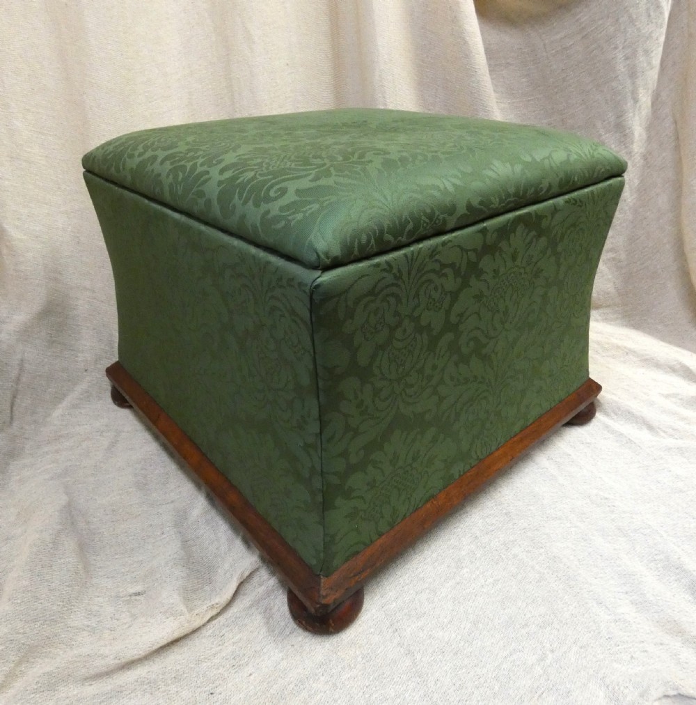 A square upholstered storage ottoman covered in green patterned damask fabric resting on a dark timber plinth base with rounded bun feet.
