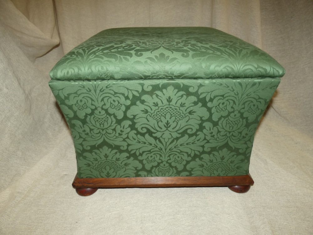 A square upholstered storage ottoman covered in green patterned damask fabric resting on a dark timber plinth base with rounded bun feet. View II