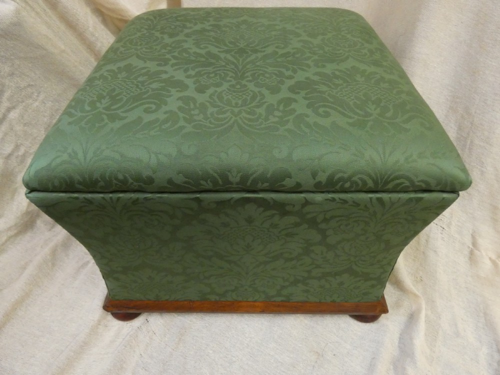 A square upholstered storage ottoman covered in green patterned damask fabric resting on a dark timber plinth base with rounded bun feet. View VI
