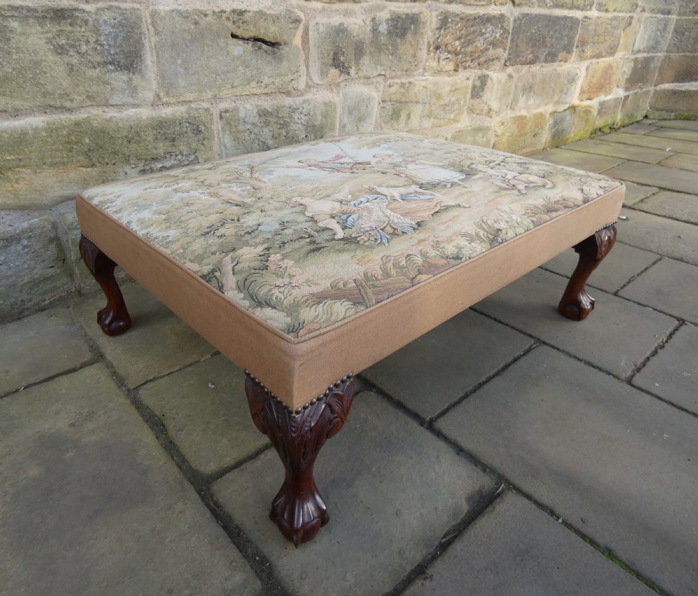 A large square upholstered centre stool featuring a tapestry top with figures in a landscape and dark carved mahogany cabriole legs with ball and claw feet. View IV